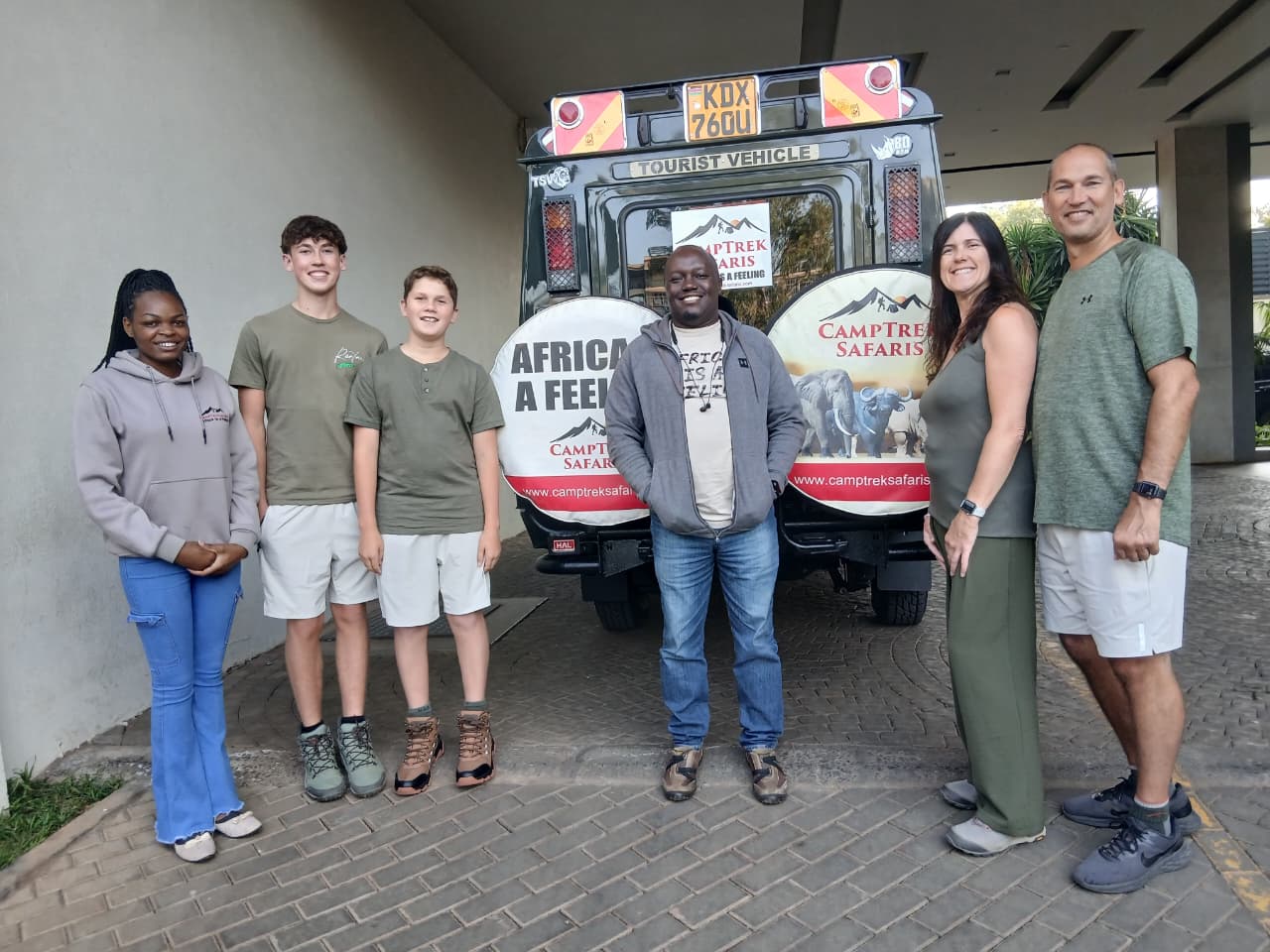 Family group posing with their CampTrek Safaris guide and tour vehicle