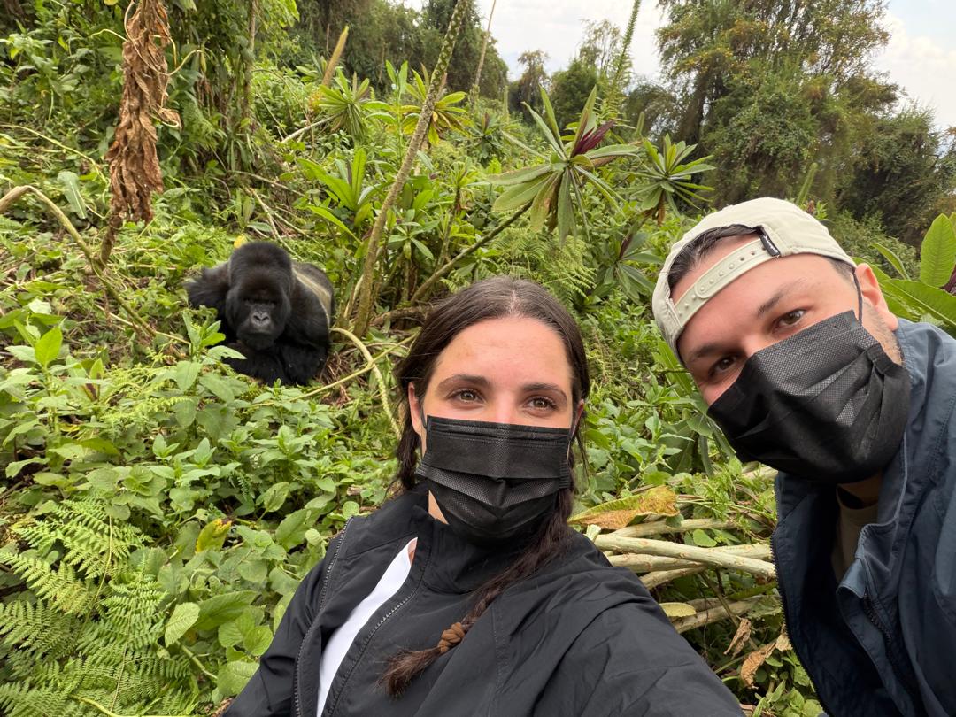 Two trekkers taking a selfie with a wild mountain gorilla visible in the background